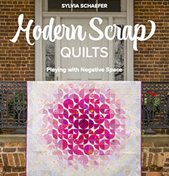 A book cover featuring a pink and white quilt draped over a railing. The title is "Modern Scrap Quilts: Playing with Negative Space" by Sylvia Schaefer